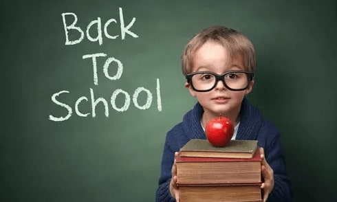 A child hodling a stack of books with a red apple on top and a sign that reads - Back to School